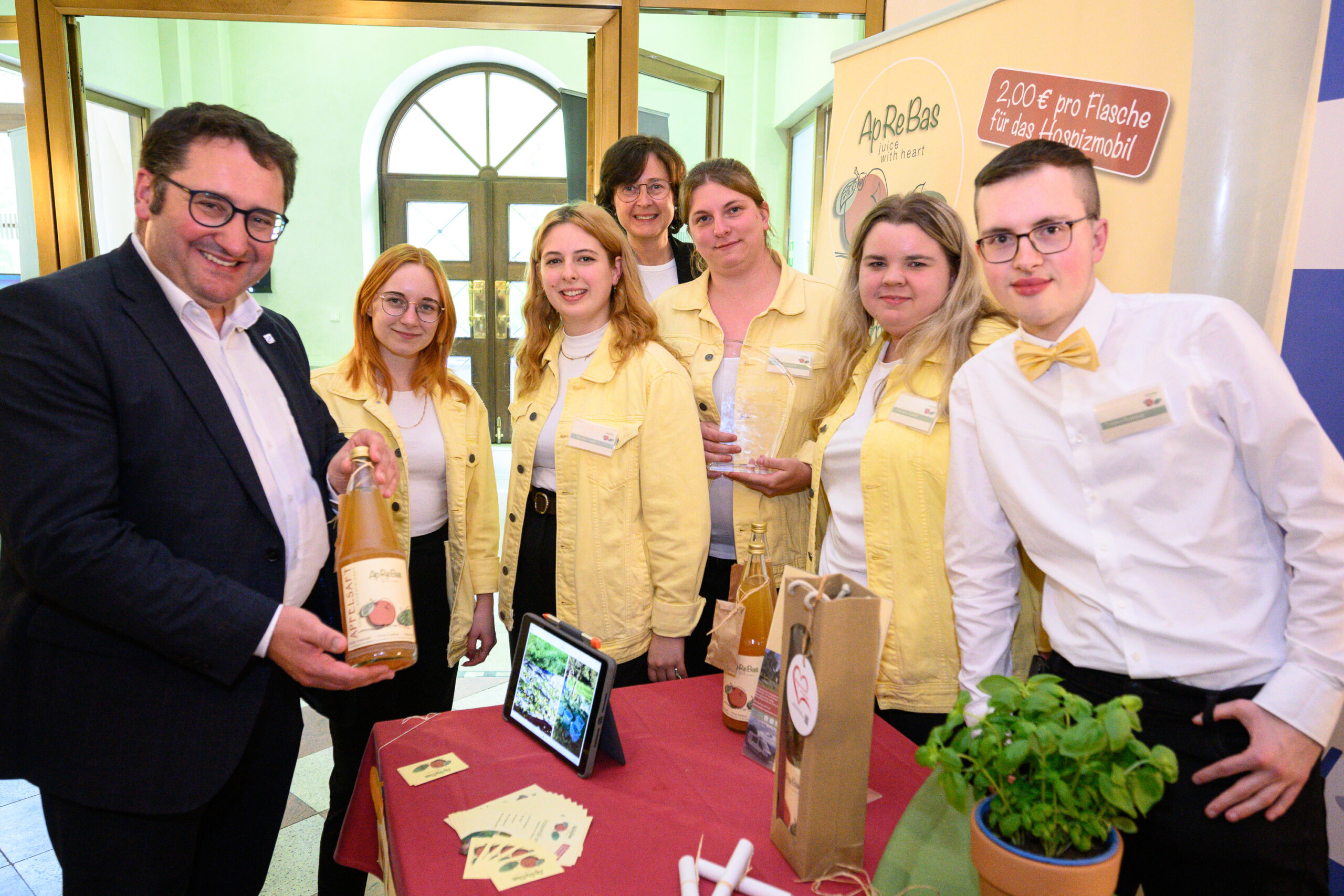 Eine Gruppe Schülerinnen und Schüler und ein Mann im Anzug stehen um einen Tisch herum.