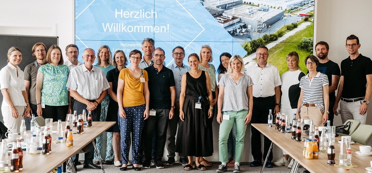 Lehrer in der Wirtschaft stehen gemeinsam vor einer großen Infowand.