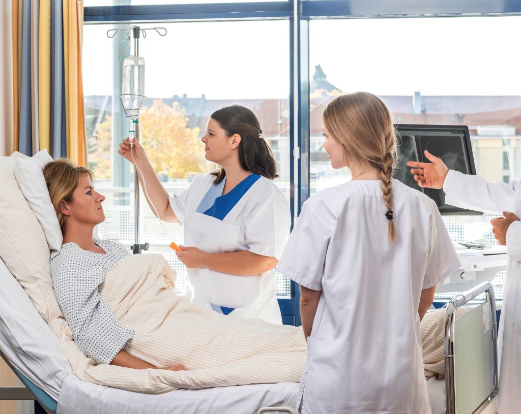 Zwei Pflegekräfte betreuen eine Frau in einem Krankenhausbett.