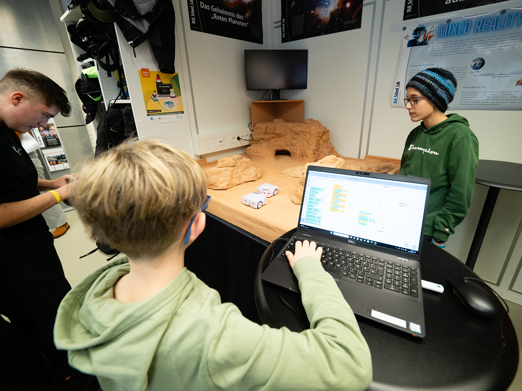 Drei Schüler codieren gemeinsam ein Wüstenfahrzeug in Miniaturformat.