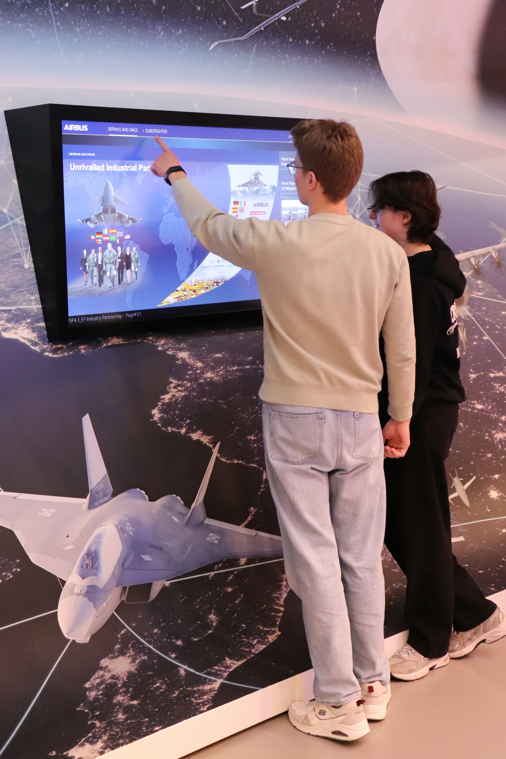 Zwei Schüler beschäftigen sich an einem Fernseher mit Airbus Defence und Space.