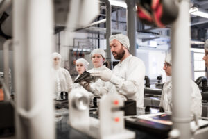 Ein Lehrer erklärt Jugendlichen in sterilen Fabrikanzügen eine Maschine in einem Labor.